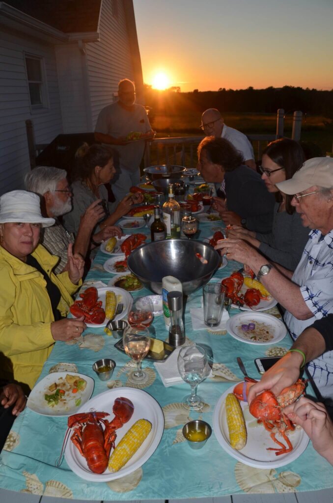 People outdoors at a table eating lobsters at sunset